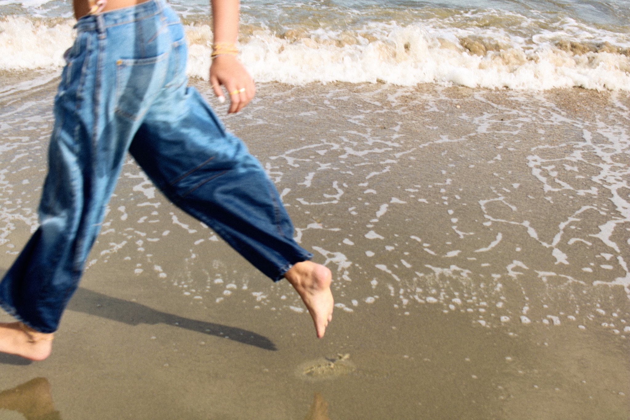 Running barefoot along the shoreline, jeans and waves